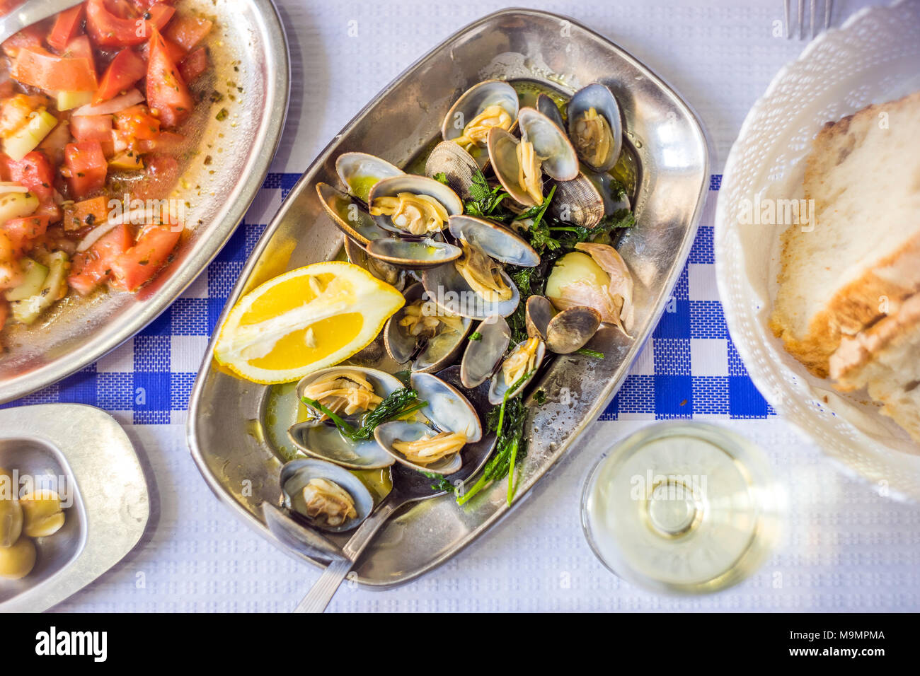 Coperti da tavola con le vongole deliziosa servita su argenteria, vino bianco, insalata di pomodoro, pane e olive da sopra, Portogallo Foto Stock