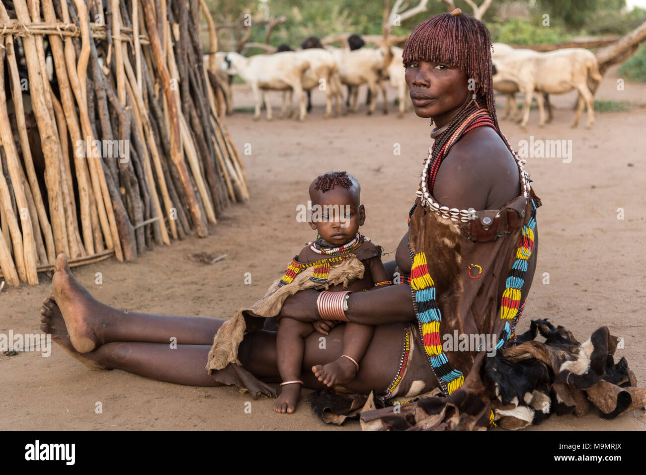 Donna con bambino seduto di fronte a capanna di fango sul terreno, Hamer tribe, Turmi, regione a sud della nazioni, Etiopia Foto Stock