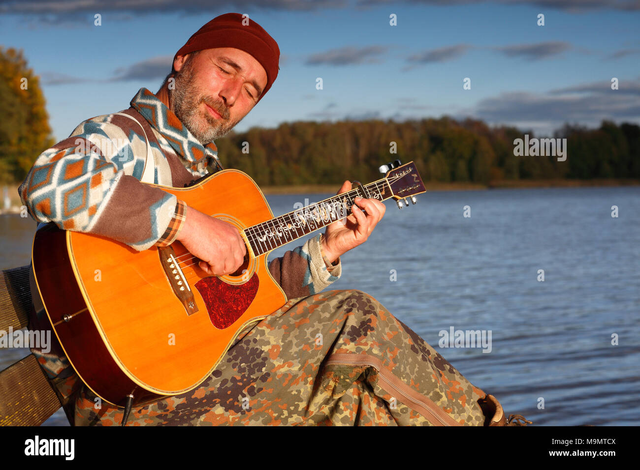 Uomo suona la chitarra su un pontile di sbarco al lago, Meclemburgo Lake District, Meclemburgo-Pomerania Occidentale, Germania Foto Stock