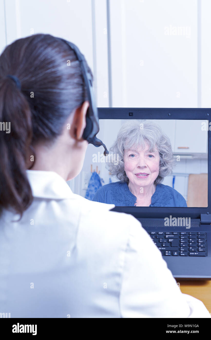 Medico donna della geriatria con la cuffia nella parte anteriore del suo portatile nel corso di una consultazione su internet con un paziente senior, concetto di telemedicina Foto Stock