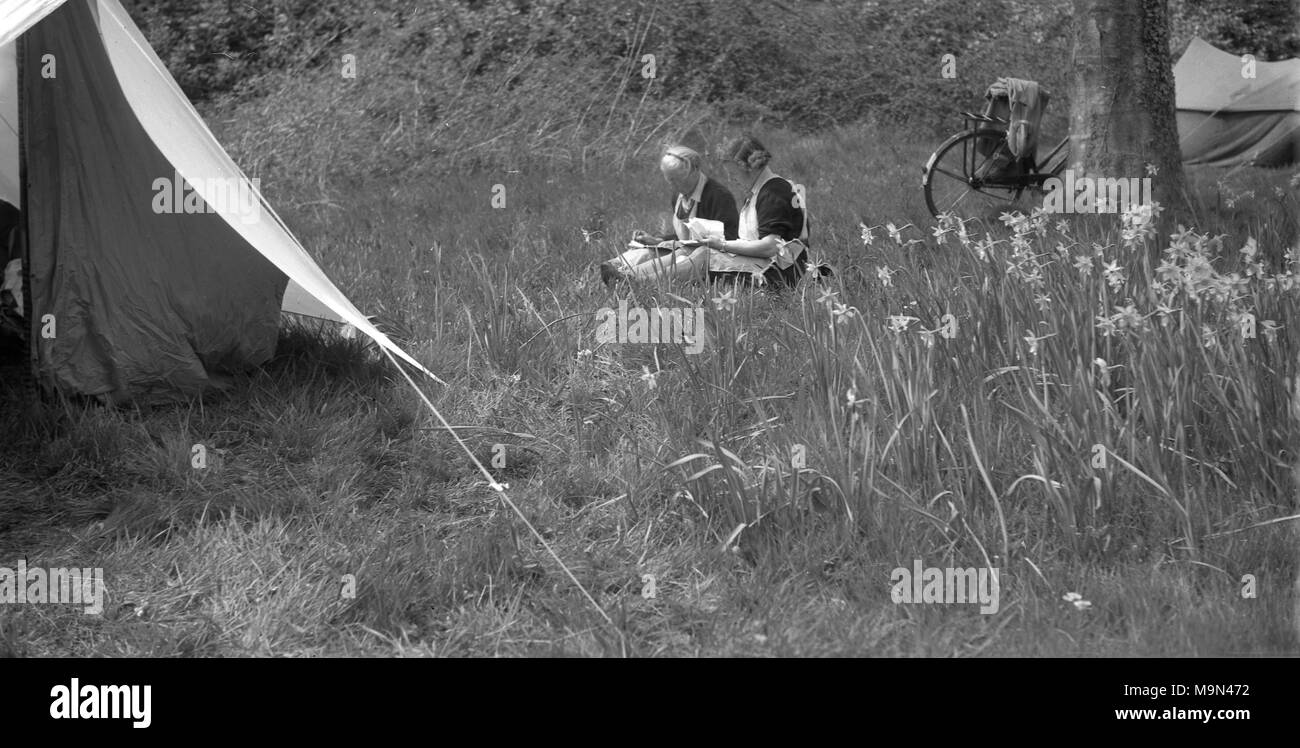 1930s, storico, due guida ragazza leader seduti in un campo erboso al di fuori della loro tenda in tela, Inghilterra, Regno Unito. Foto Stock