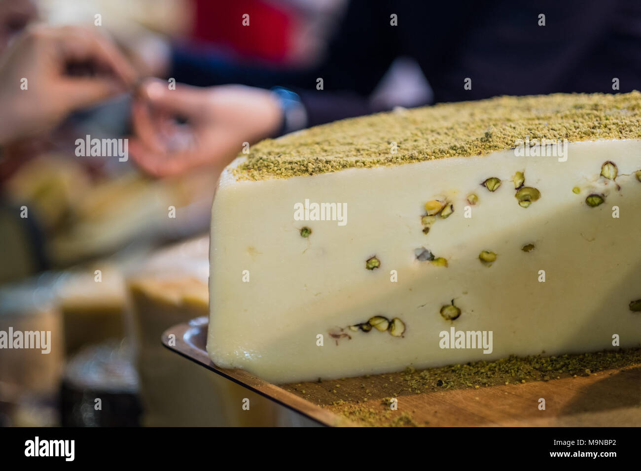 Delizioso formaggio ruota con i pistacchi sul vassoio in legno nel negozio di delicatessen con il fornitore e cliente in background Foto Stock