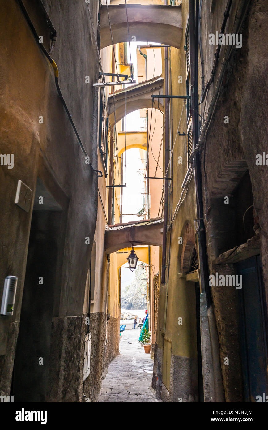 Stretto vicolo buio in un italiano medievale città tradizionale con luce proveniente dalla fine, porte sulle pareti laterali e lanterna appeso al di sotto di un arco Foto Stock