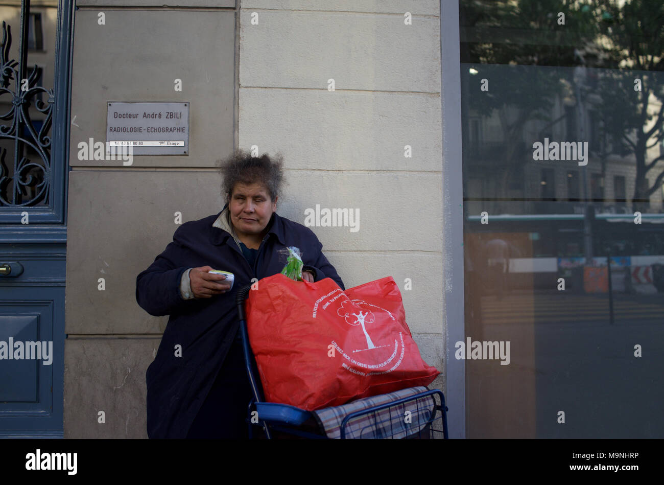 Senzatetto donna seduta su strada con grande sacchetto rosso - Boulevard Barbès, Parigi, Francia Foto Stock