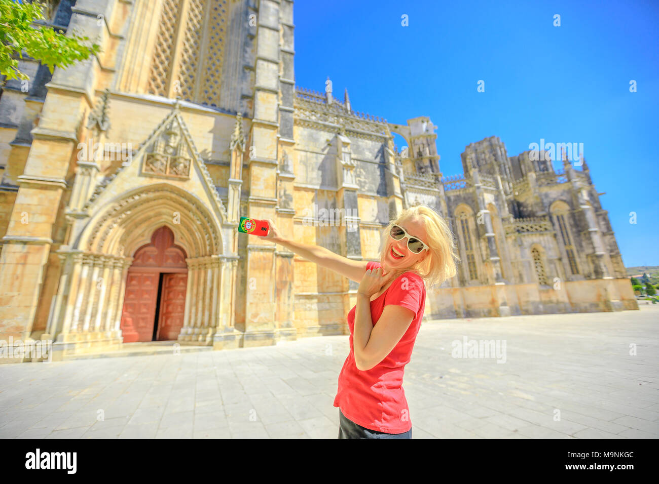 Donna Felice Tiene la foto del Monastero di Batalha uno dei più importanti siti di gotica in Portogallo. Stile di vita femminile prende le immagini dal telefono cellulare con la bandiera del Portogallo coperchio.Turismo e viaggi in Portogallo Foto Stock