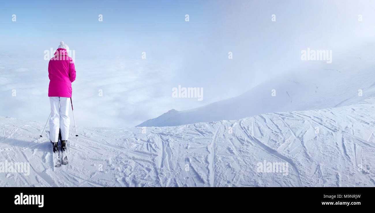 Donna sciatore in rosa Giacca sci sul bordo della collina ripida con nulla solo nuvole di fronte a lei. Sedlo Lomnicke ski resort, Slovacchia Foto Stock