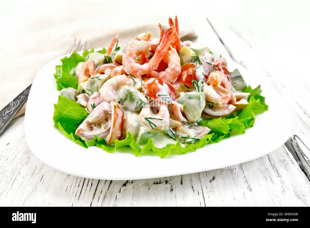 Con insalata di gamberetti, avocado, pomodori e maionese sul verde lattuga in una piastra, igienico, forcella sullo sfondo del tavolo in legno Foto Stock
