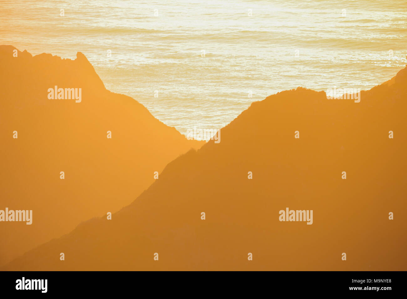 Tramonto su acque oceaniche si illumina le colline e le montagne con sfumature e tonalità di golden, ambra e luce arancione in Big Sur, California. Foto Stock