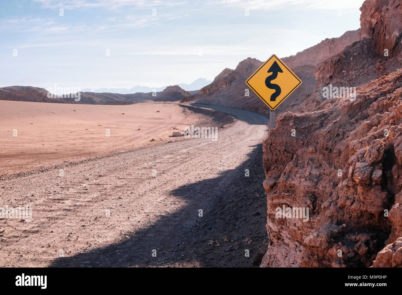 Una strada tortuosa in un paesaggio desertico con un giallo strada segno. Foto Stock