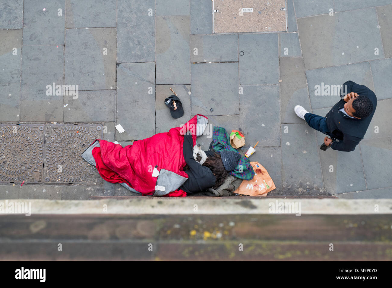 Guardando verso il basso su un senzatetto dormire con il suo cane al di fuori di una stazione della metropolitana mentre un altro uomo cammina passato. Londra, Regno Unito Foto Stock