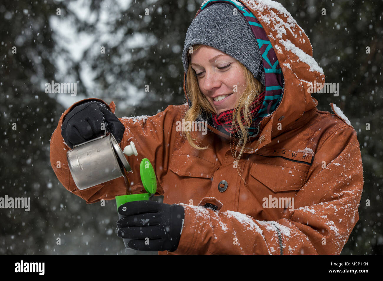 Donna versando caffè fatto sul fornello da campeggio nella tazza in inverno, Sureanu, Romania Foto Stock