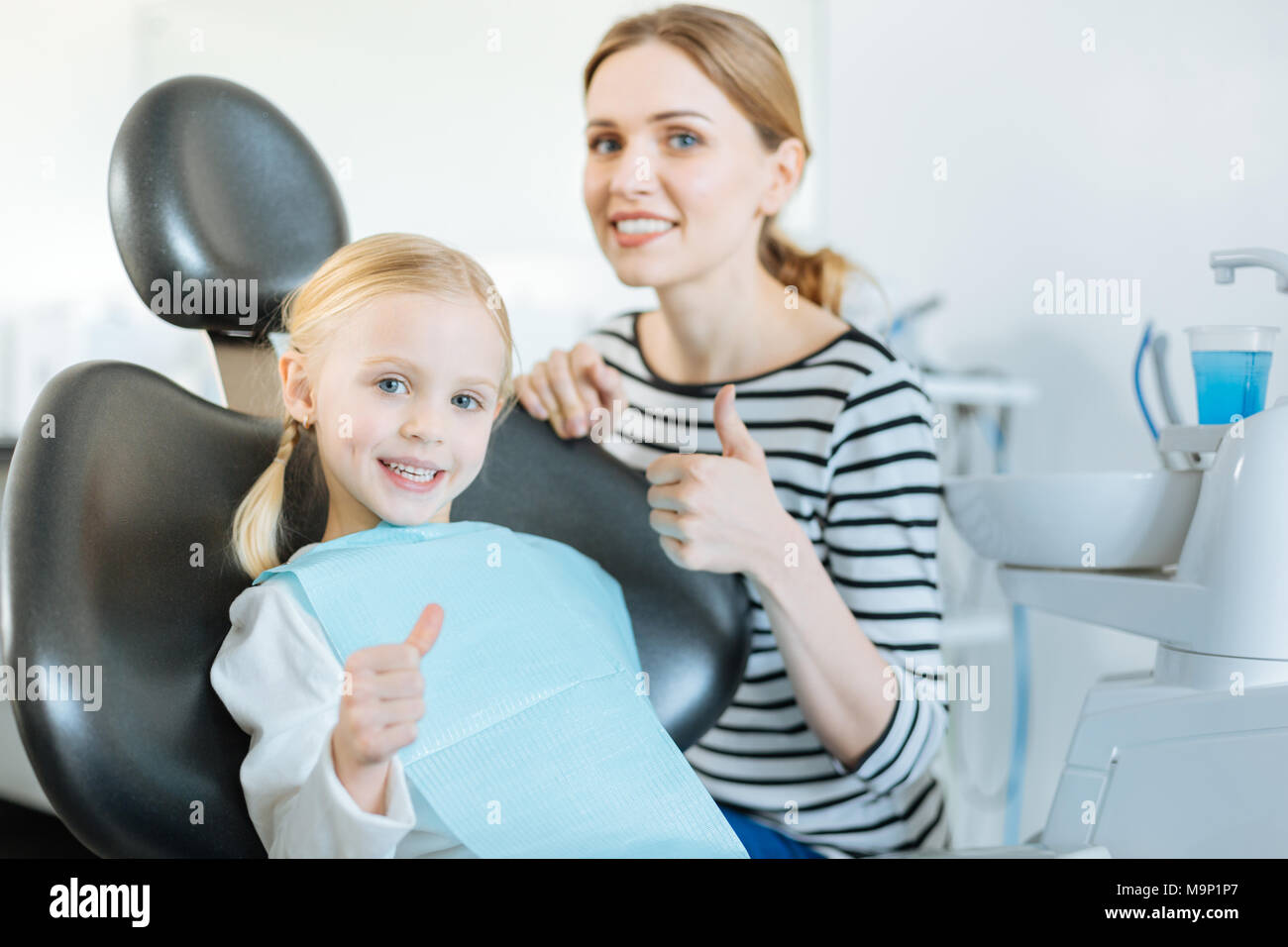 Carino ragazza e sua madre che mostra i pollici fino a dentisti office Foto Stock