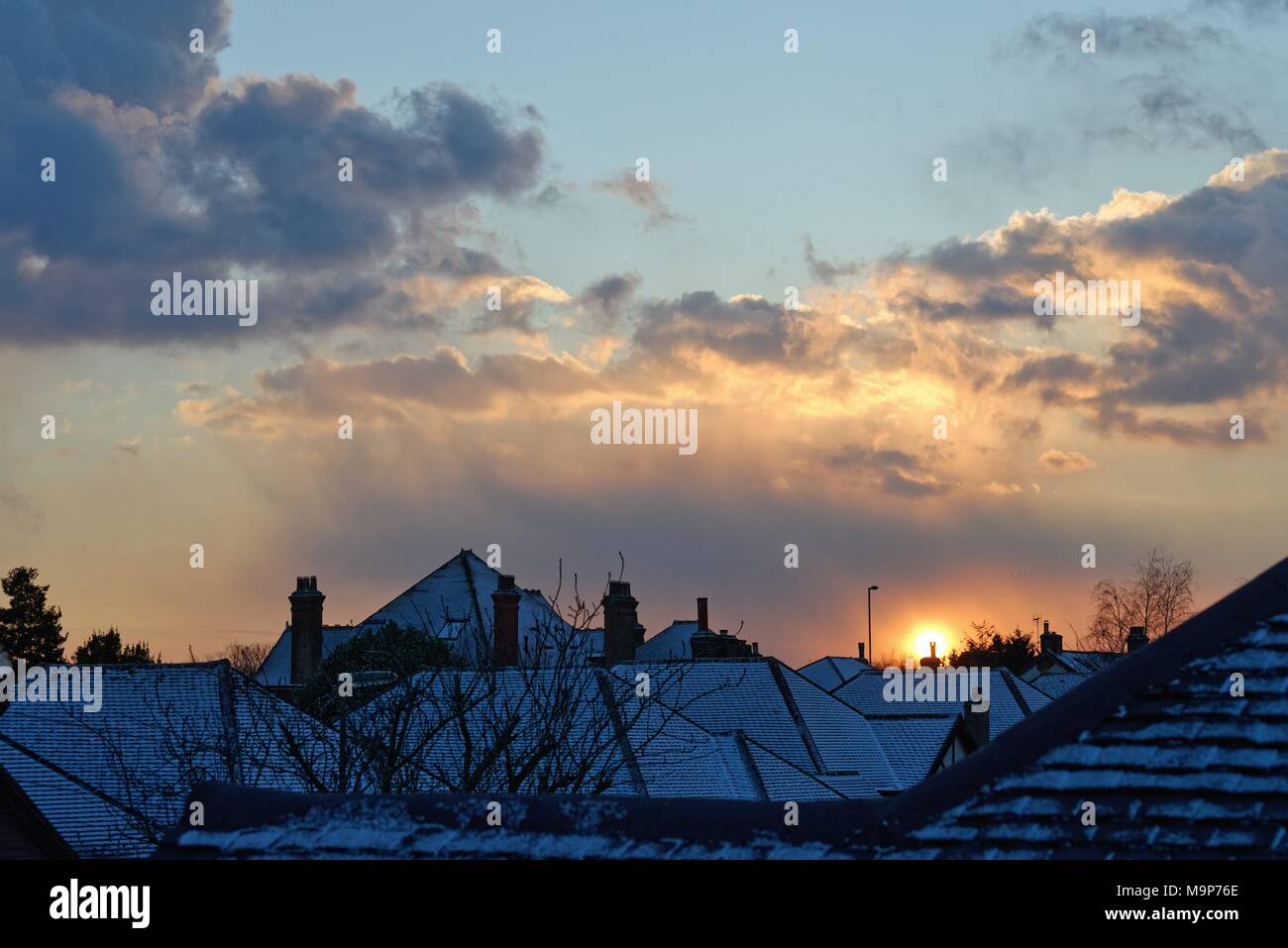 Tramonto spettacolare attraverso la raccolta di nuvole di neve su tetti suburbana Foto Stock