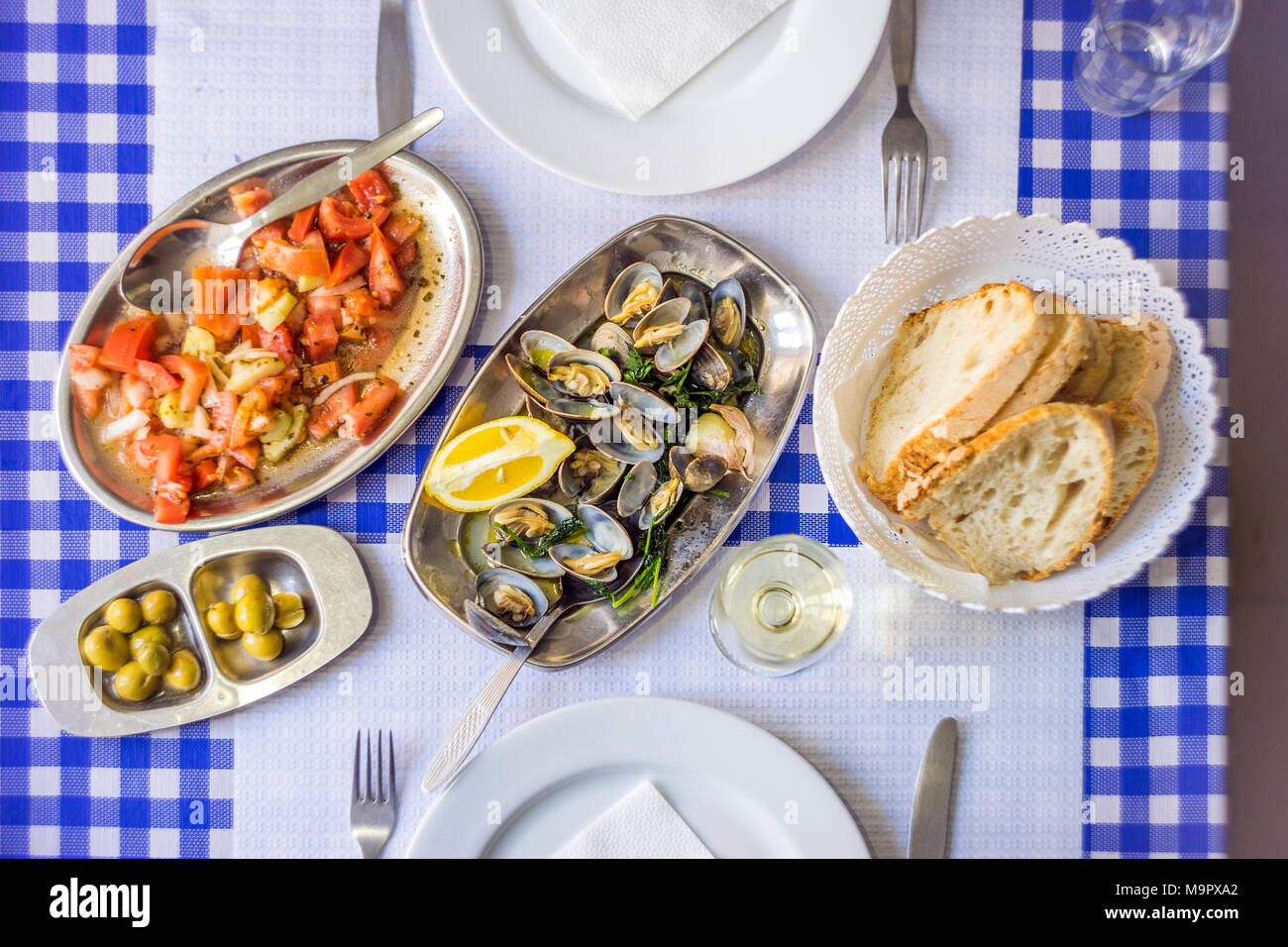 Coperti da tavola con le vongole deliziosa servita su argenteria, vino bianco, insalata di pomodoro, pane e olive da sopra, Portogallo Foto Stock