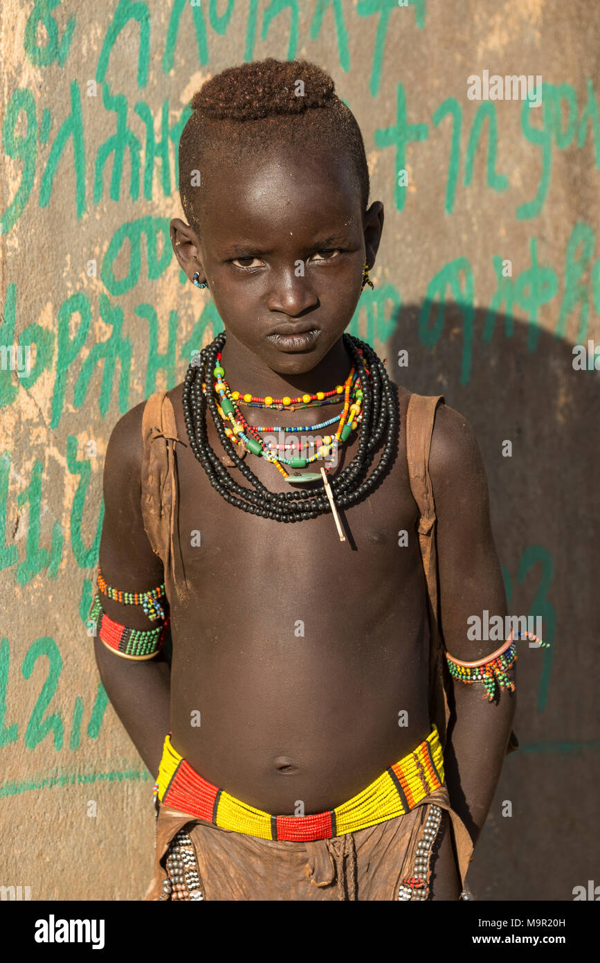 Ragazzo di circa 9 anni, posa con un grave colpo d'occhio di fronte ad una parete colorata, Hamer tribe, Turmi mercato, Southern Foto Stock