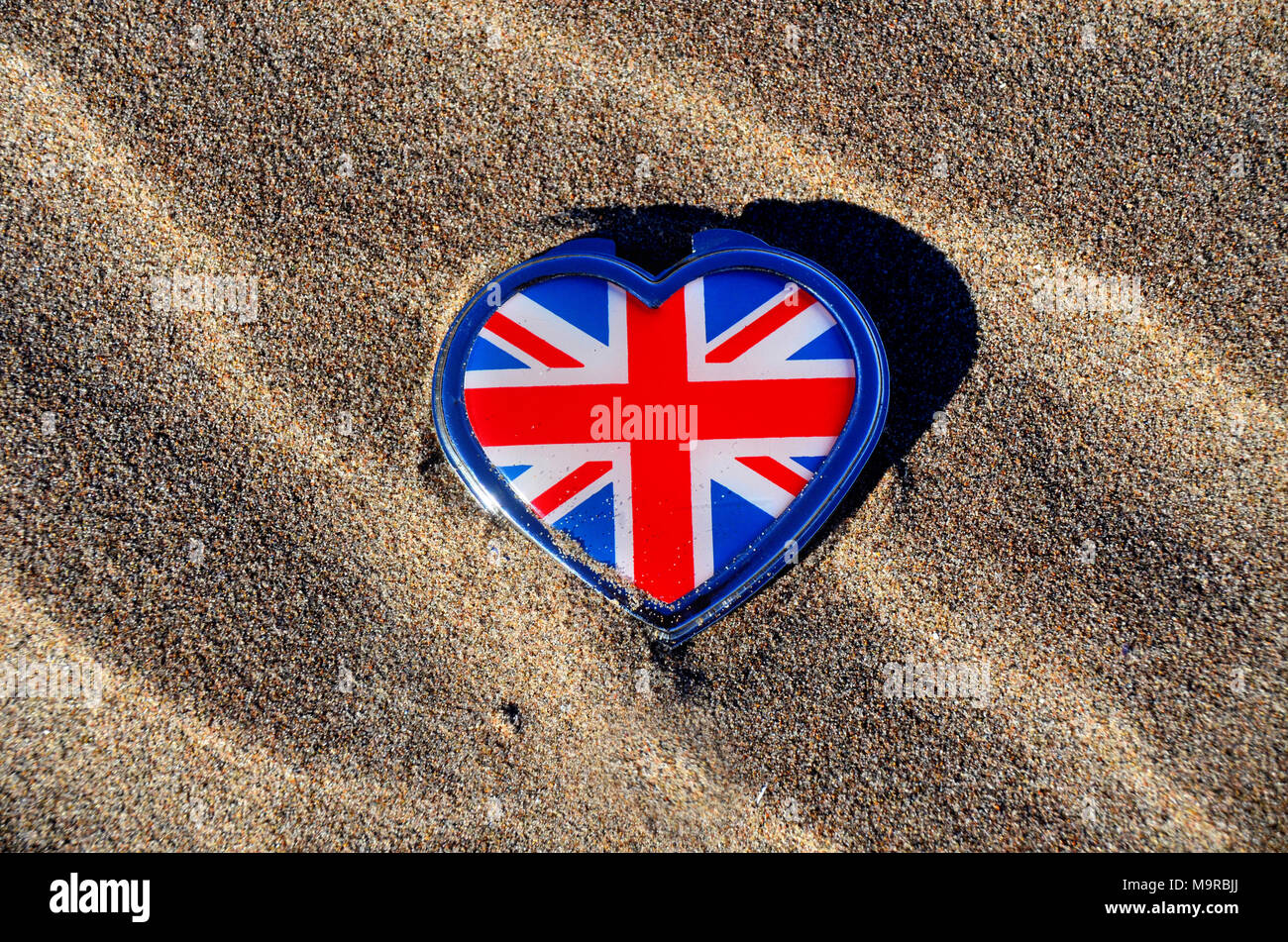 Un union jack di copertura a heart-shaped tin giacente su una sabbiosa spiaggia modellato. Foto Stock