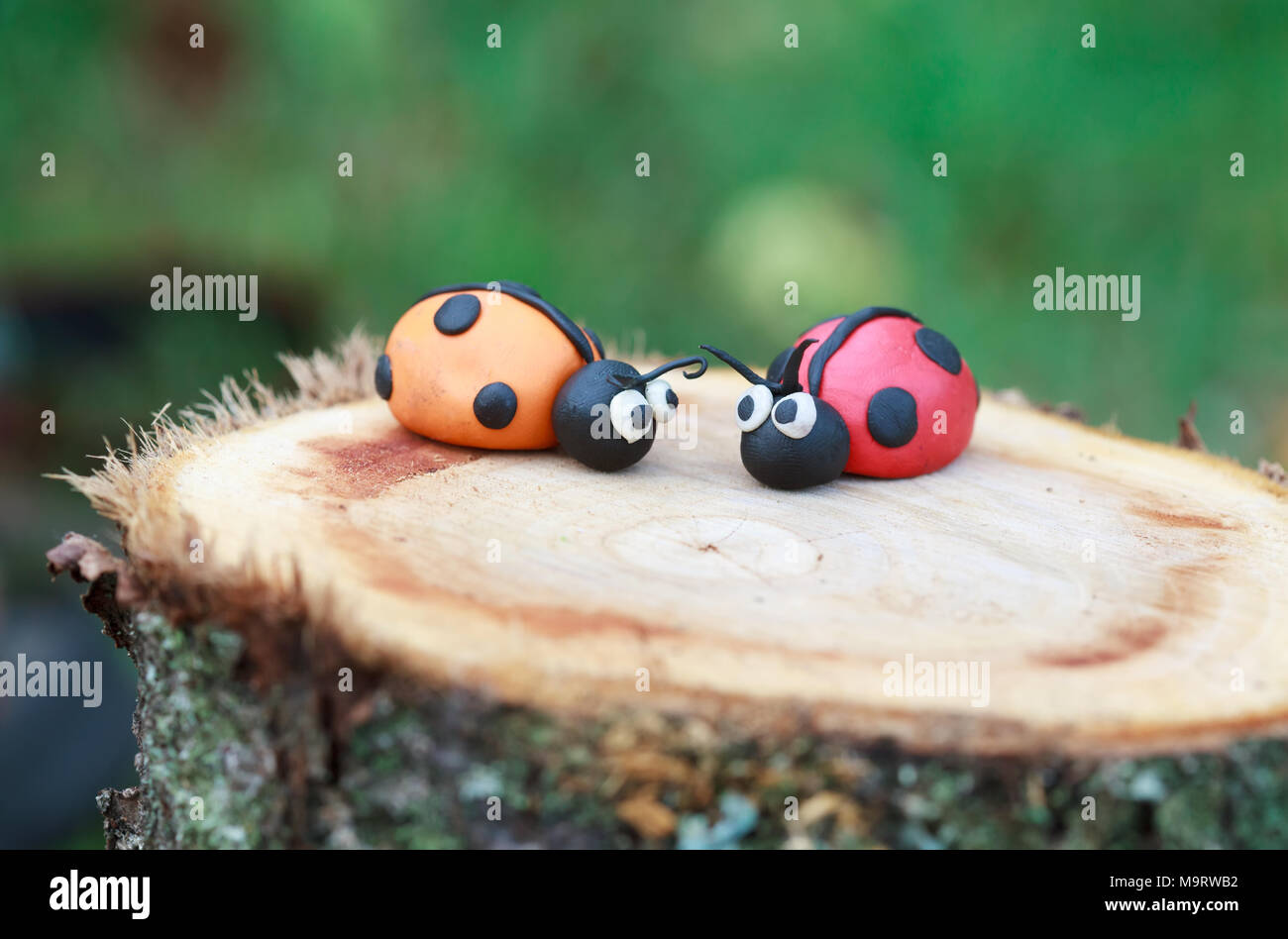 Plastilina world - poco in casa rosso e arancio ladybugs seduto su un vecchio ceppo, il fuoco selettivo Foto Stock