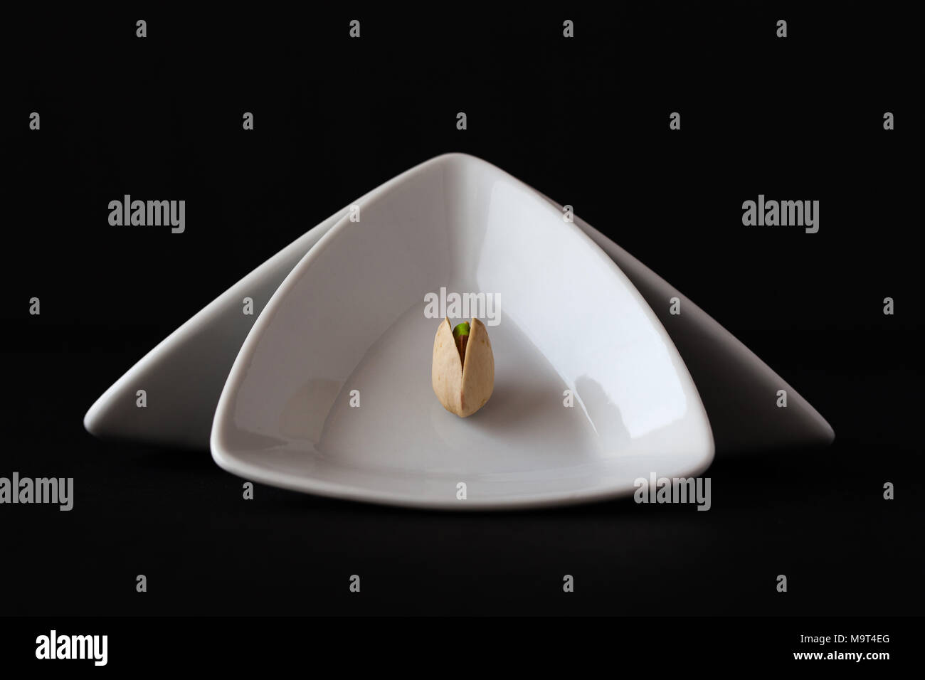 Bianco triangolare di coppe in ceramica con pistacchio su sfondo nero. Cibo scure della fotografia. Foto Stock