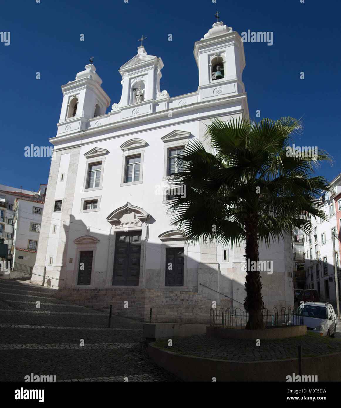 Chiesa di San Miguel dietro a un albero di palma e le strade in ciottoli nel distretto di Alfama, il più famoso e antico quartiere tipico di Lisbona. Portogallo Foto Stock