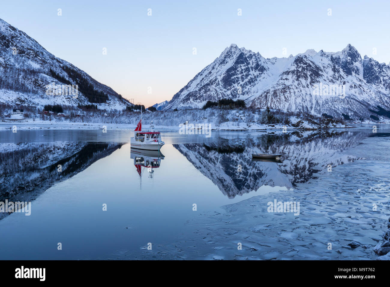 Barca sul fiordo di calma. Paesaggio invernale con montagne innevate e riflessi in acqua e ghiaccio Foto Stock