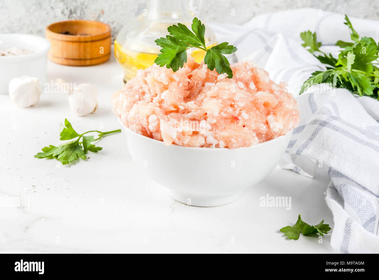 Il pollo crudo o in Turchia le carni macinate in bianco ciotola con olio, le spezie e le erbe su sfondo chiaro. Copia dello spazio. Foto Stock