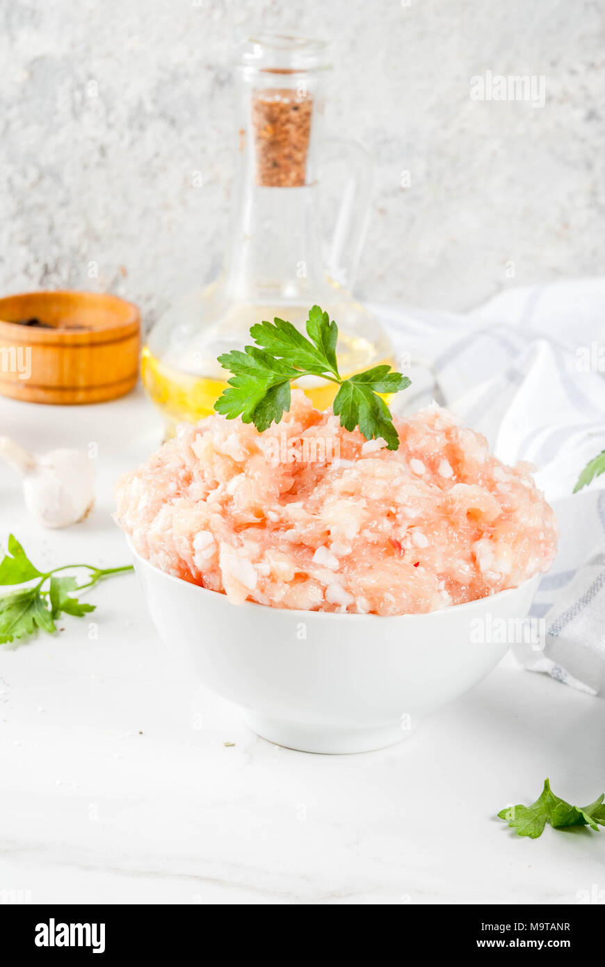 Il pollo crudo o in Turchia le carni macinate in bianco ciotola con olio, le spezie e le erbe su sfondo chiaro. La copia verticale dello spazio Foto Stock