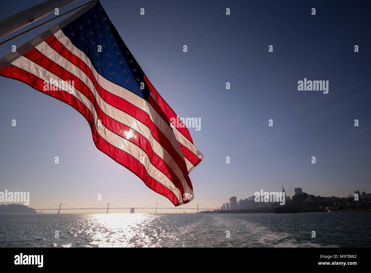 La bandiera americana, stelle e strisce, da Alcatraz ferry boat con la Baia di San Francisco, la città e la Oakland Bay Bridge in background. Foto Stock