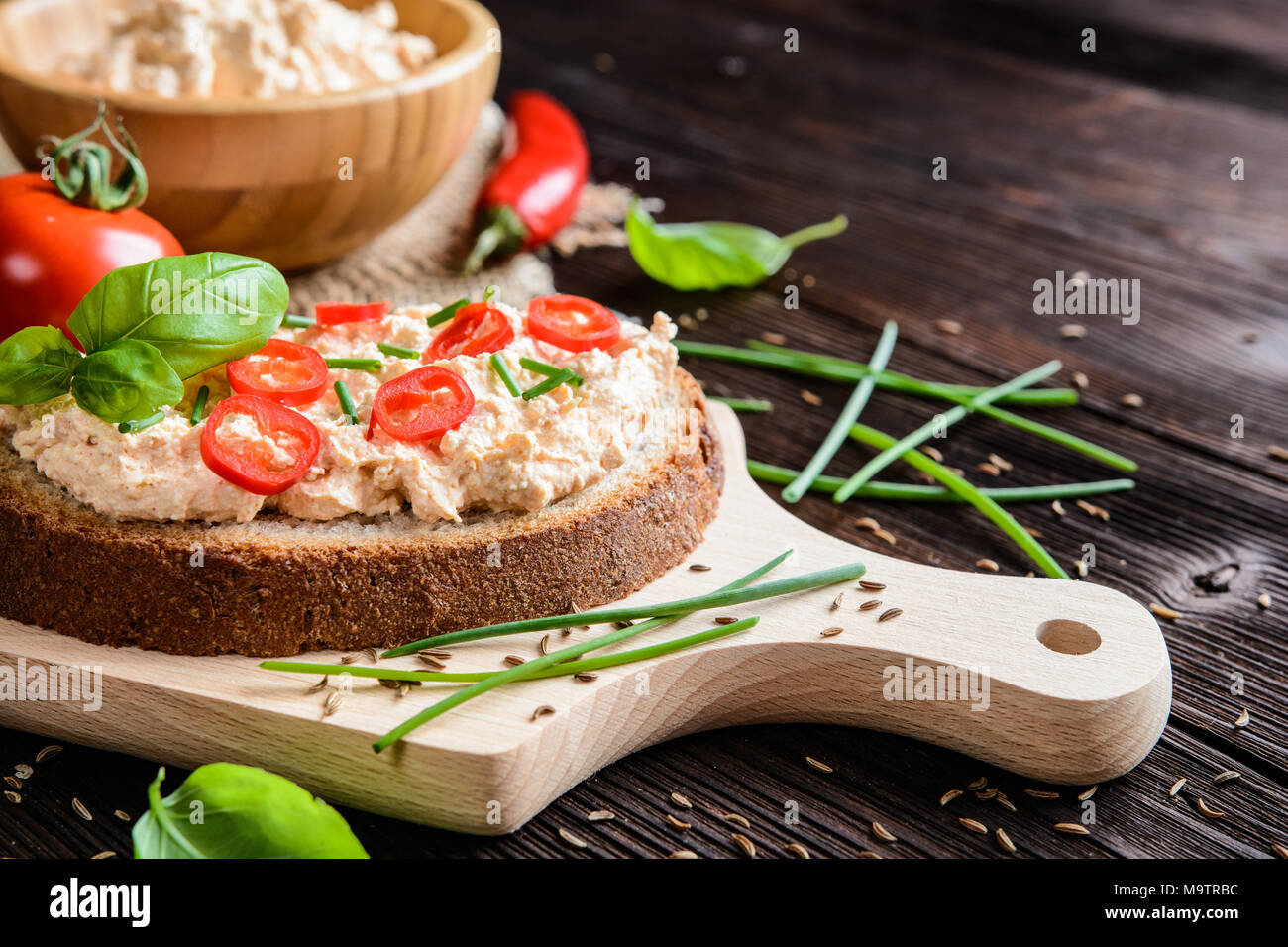 Una fetta di pane con il peperoncino cagliata diffusa con cumino in polvere, erba cipollina e basilico Foto Stock
