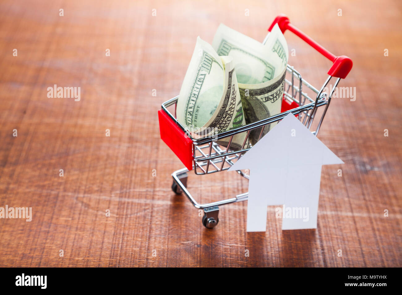 I soldi in un negozio di carrello e una casa su un sfondo di legno.. Acquisto di una proprietà. Foto Stock