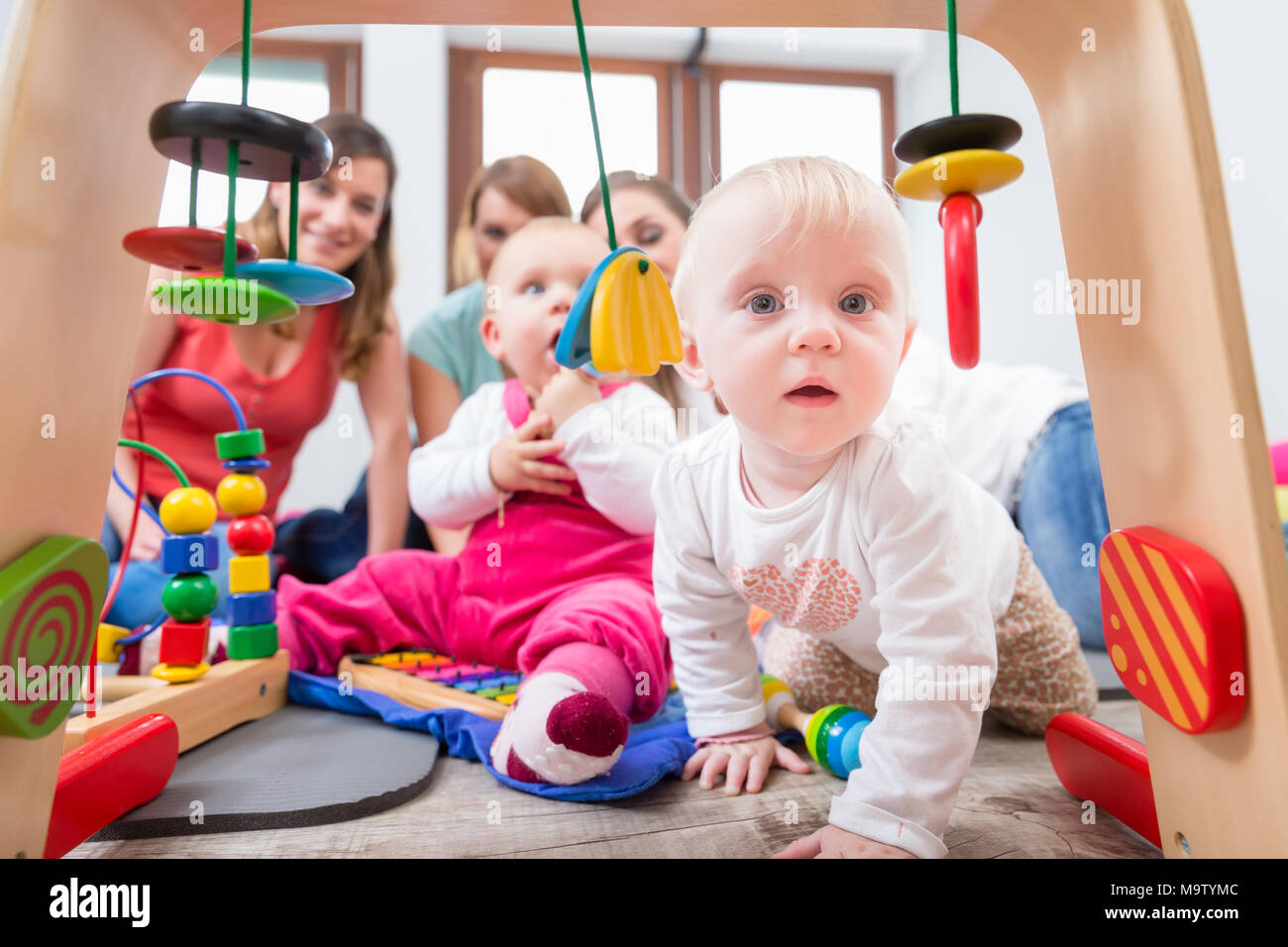 Carino Baby girl mostra curiosità cercando di raggiungere i giocattoli multicolore Foto Stock