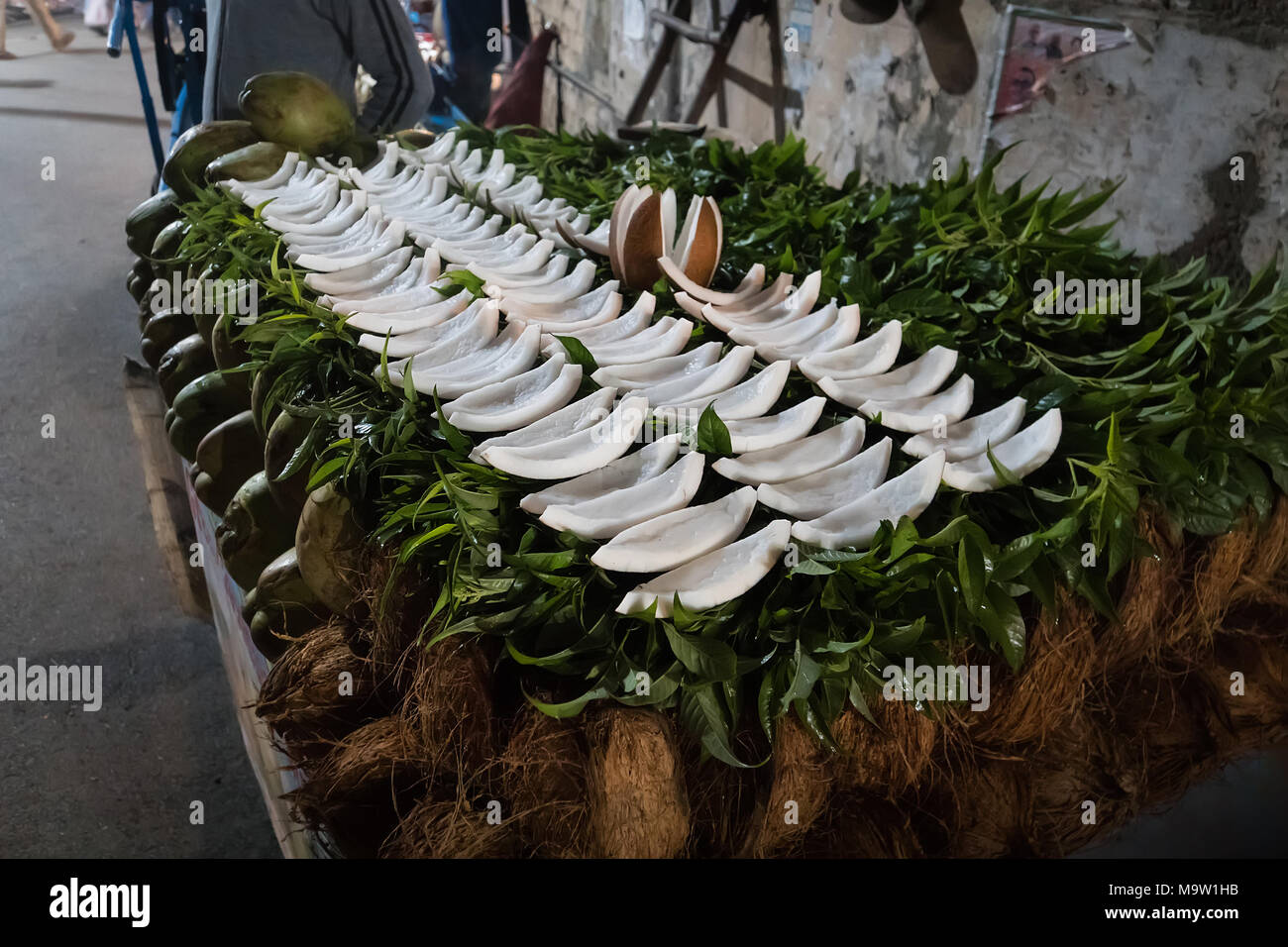 Una noce di cocco tagliata in porzioni giacciono sul contatore di un venditore ambulante. Notte tempo. La cucina di strada. Pila di noce di cocco per la vendita nel mercato Foto Stock