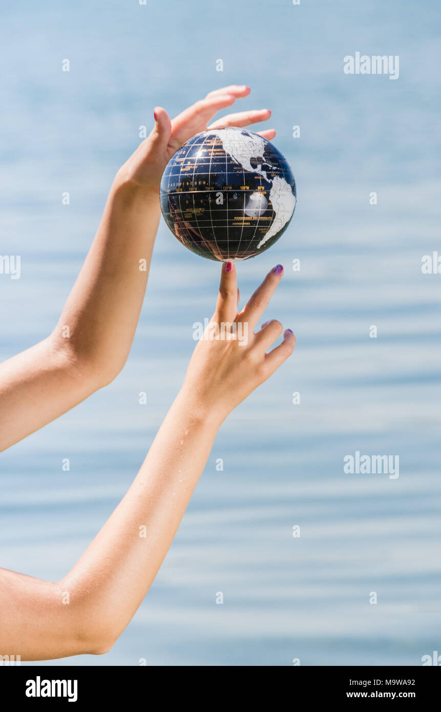 Mani di una giovane donna di bilanciamento di massa sul suo dito - sfera di acqua che mostra vari continenti Foto Stock