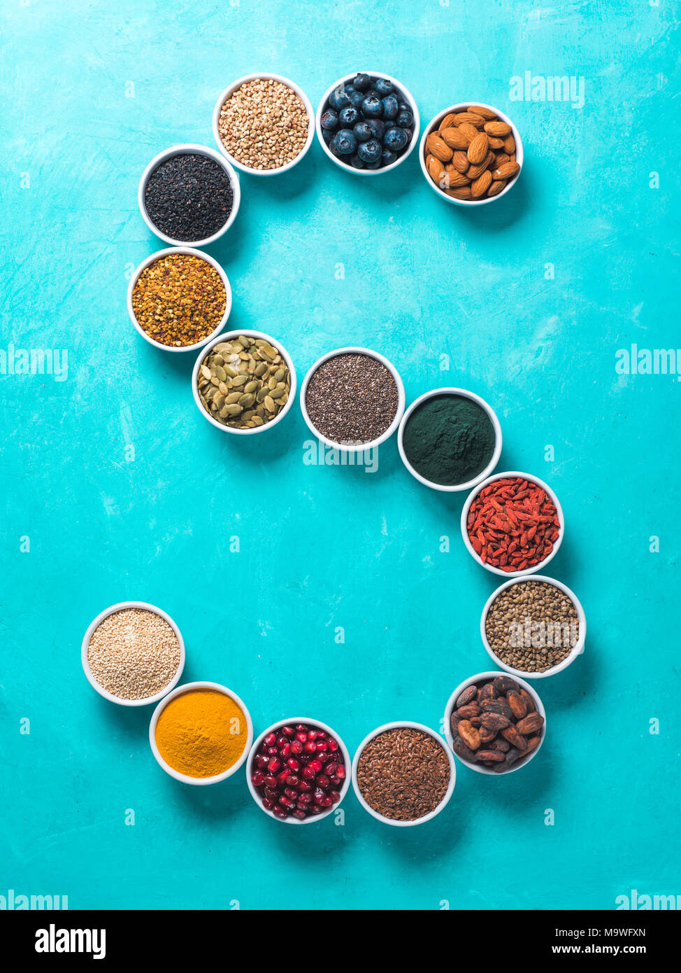 Al di sopra di vista di vari superfoods in piccolo vaso in forma S lettera su sfondo blu.Super come chia,spirulina,fava di cacao,goji,canapa,mirtillo,la quinoa,essere Foto Stock