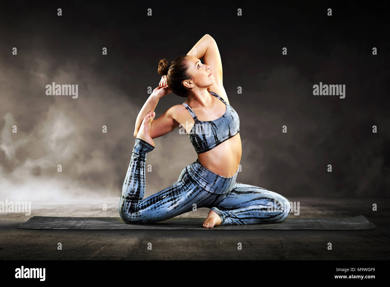 Giovane donna facendo un piccione pongono durante un allenamento di yoga su un tappeto in un vicino la vista laterale in una salute e concetto di fitness Foto Stock