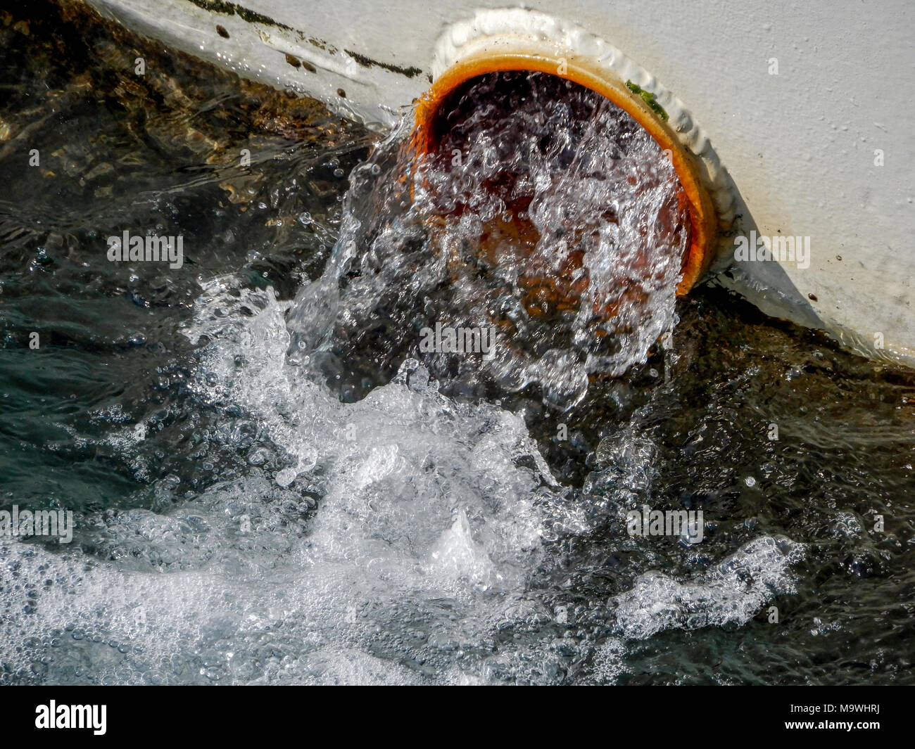 L'acqua fluisce dal tubo sullo scafo di una nave, vicino. Foto Stock