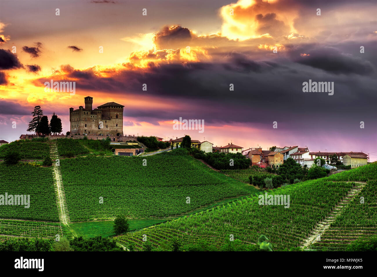 Un tramonto spettacolare cielo sovrasta il villaggio di Grinzane Cavour con il suo castello (Unesco W. H. S.) circondato da vigneti nelle Langhe piemontesi. Foto Stock