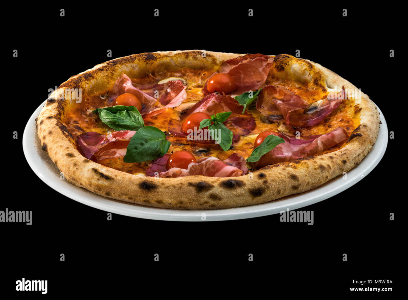 Pizza con pomodori ciliegia, prosciutto e basilico isolati su sfondo nero Foto Stock