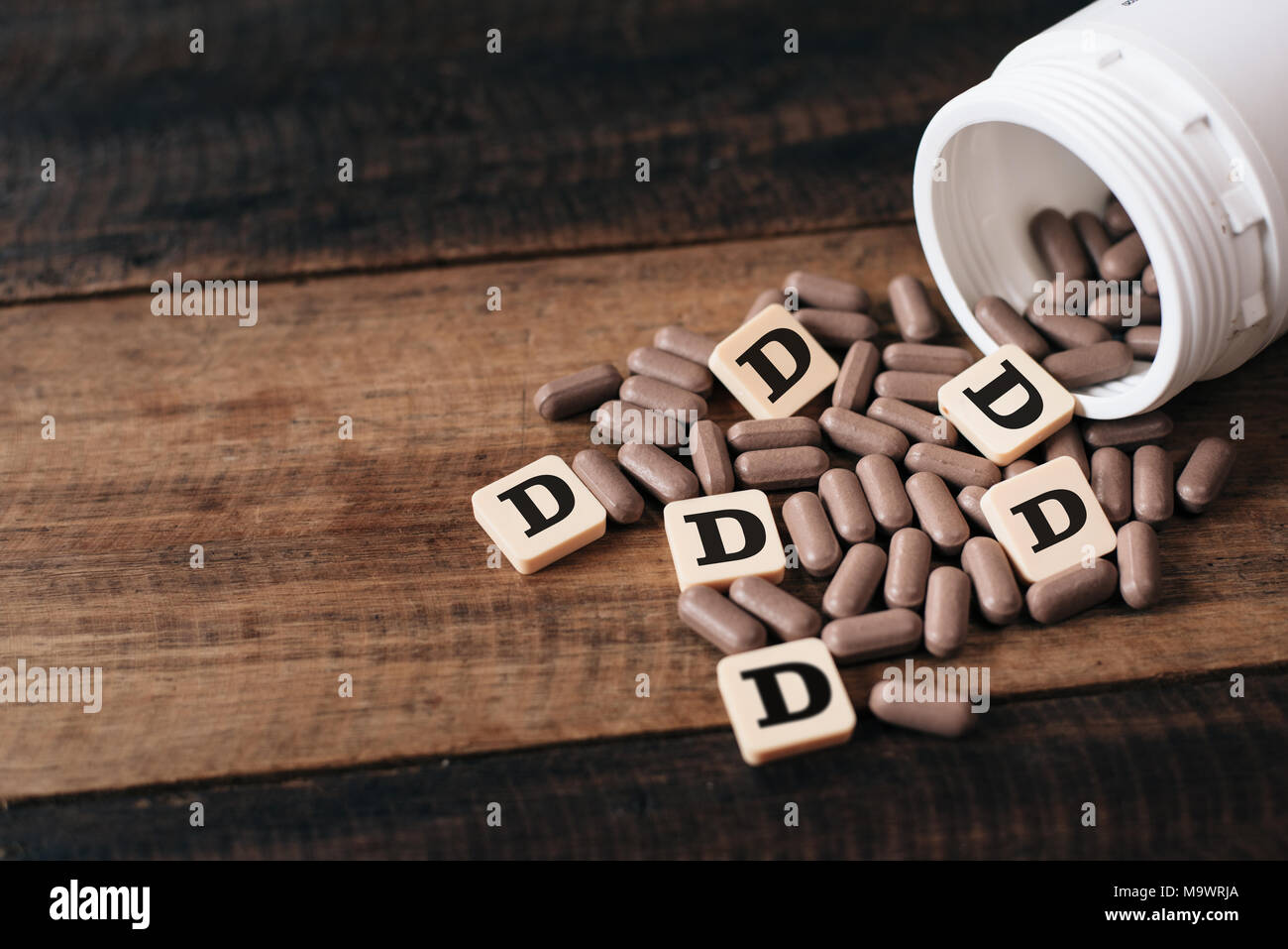 La vitamina D pillole e la bottiglia sul tavolo di legno con piastrelle alfabeto lettera scritta D. sanitari e medici concetto Foto Stock