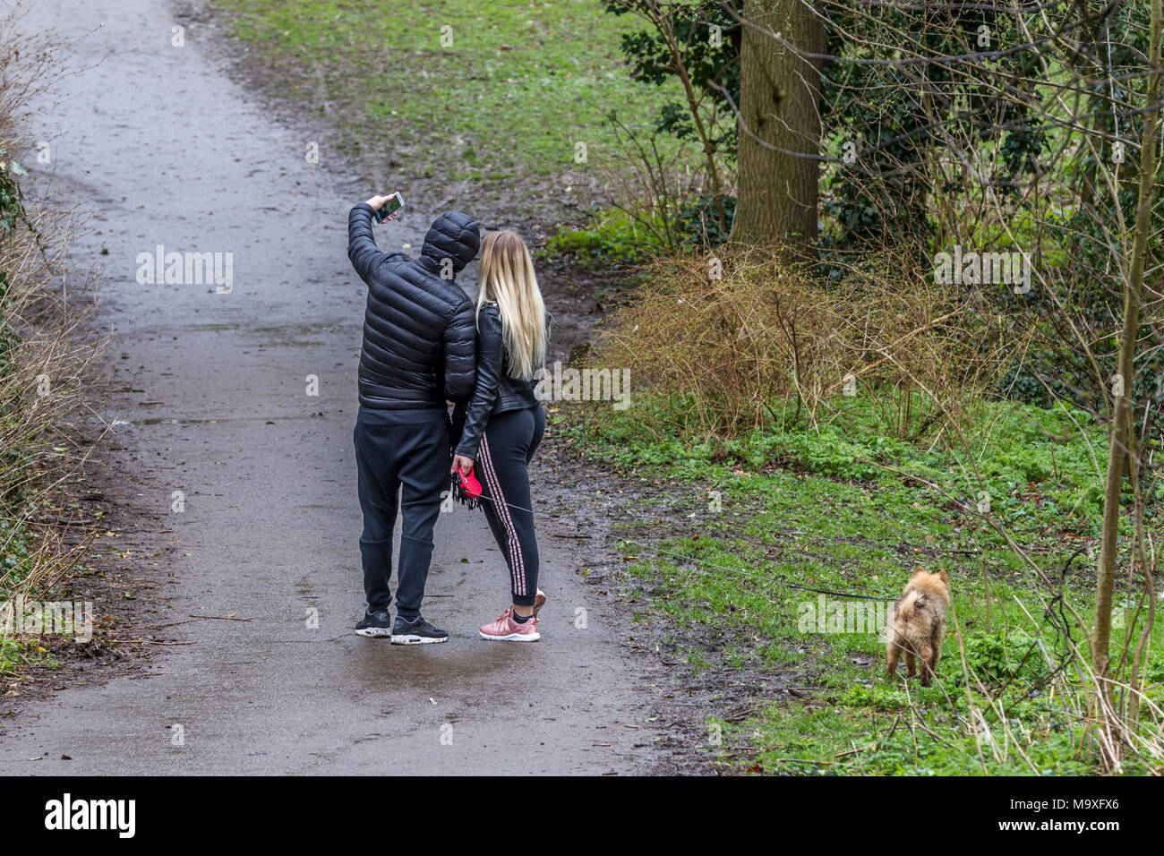Northampton. U.K. Il 29 marzo 2018. Meteo. Un giovane a spasso il loro cane piccolo, si ferma a prendere un selfie. Credito: Keith J Smith./Alamy Live News Foto Stock