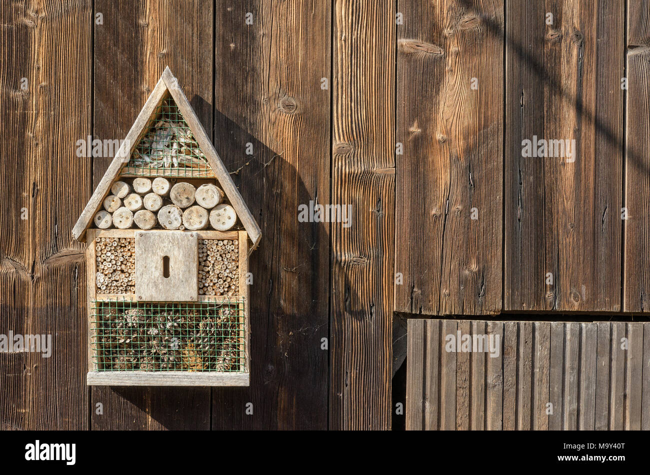 Un vecchio hotel di insetto appeso su un fienile in legno porta in campagna Foto Stock