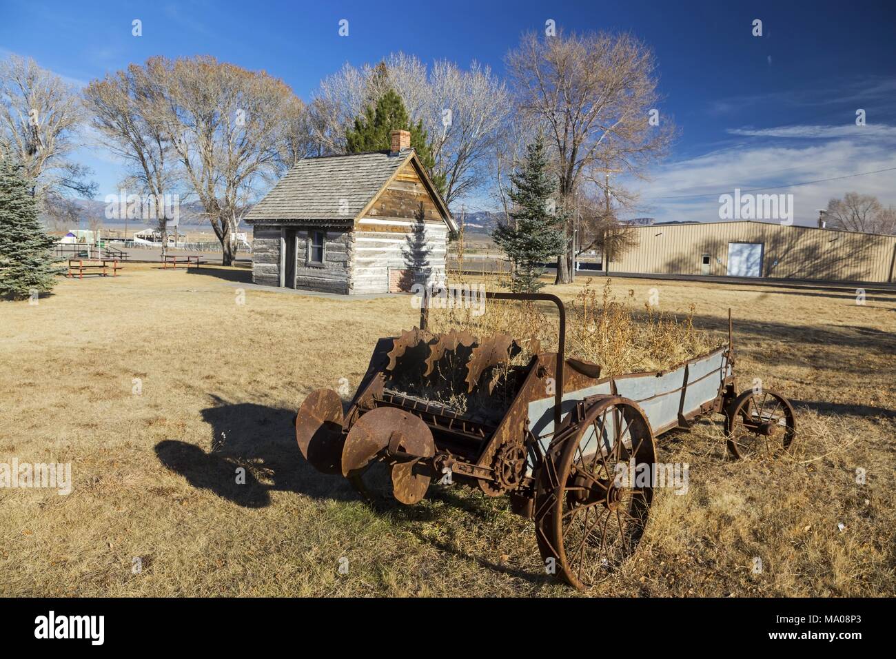 Carro arrugginito ruota nella parte anteriore del vecchio West Selvaggio Log Cabin in Mormon Pioneer Heritage Park, Scenic Highway 89 vicino alla città di Panguitch, Utah Foto Stock