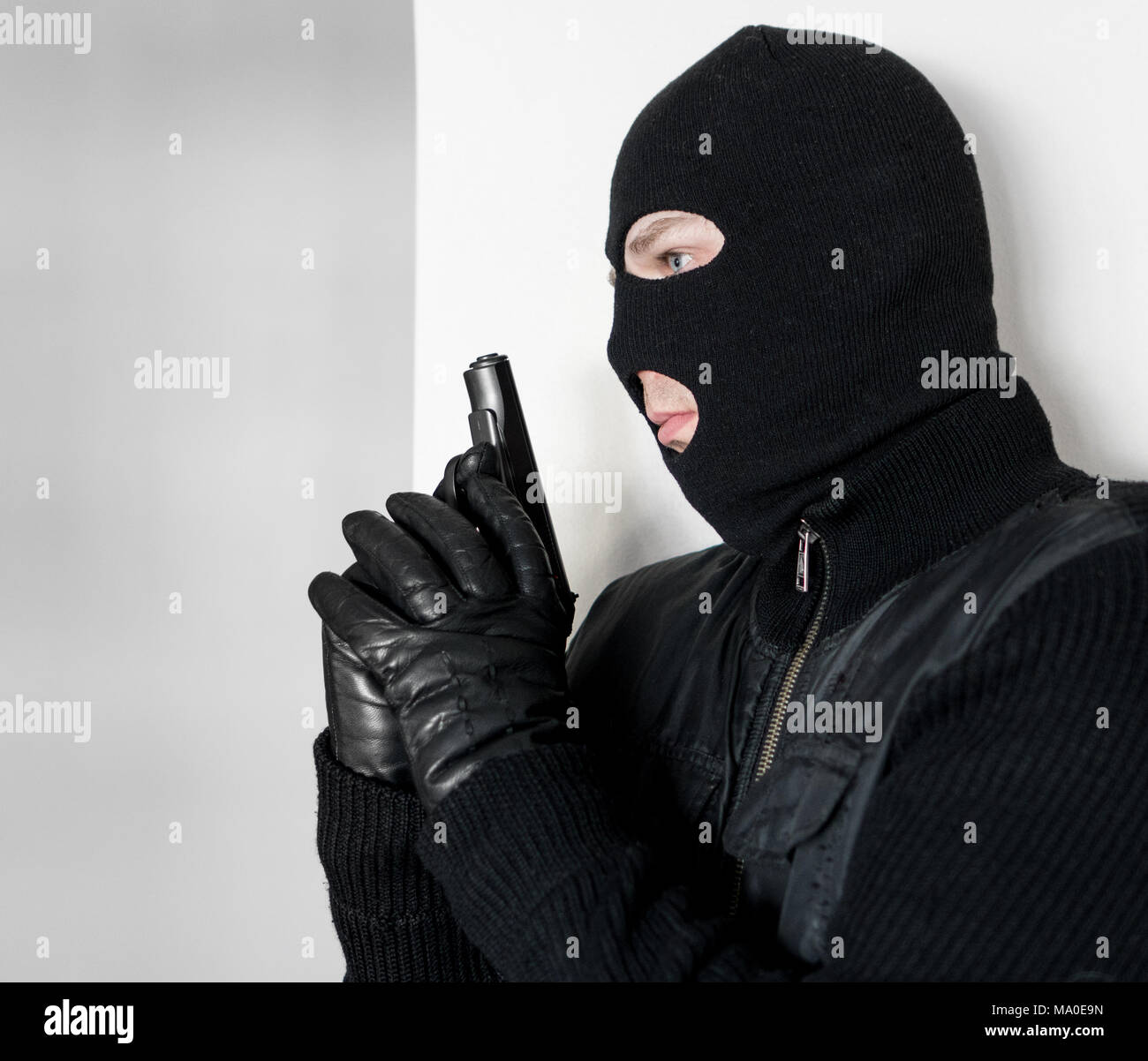 Uomo armato in passamontagna nascosto dietro un muro Foto stock