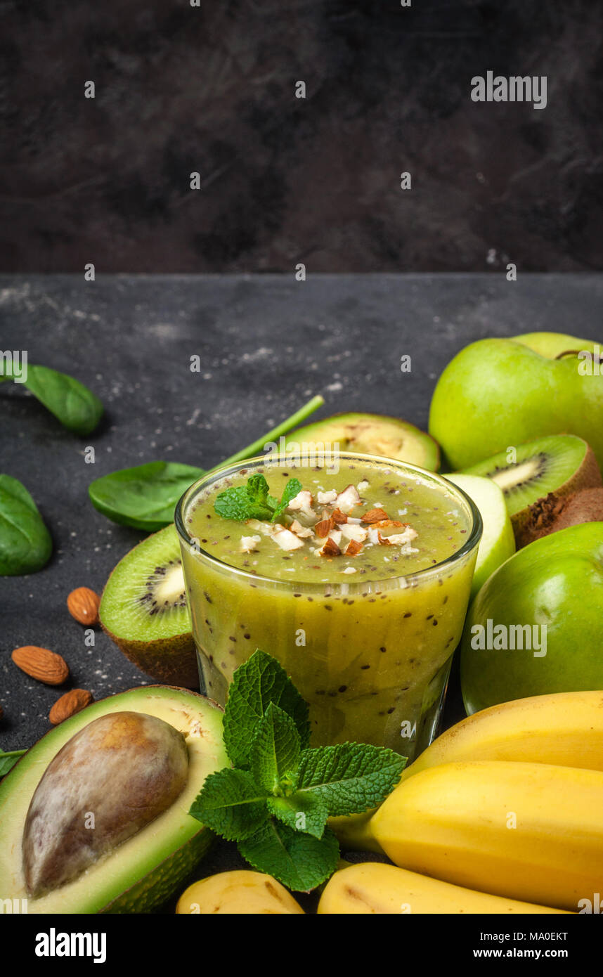 Un sano frullato verde e gli ingredienti su sfondo scuro. Frullato di kiwi con frutti di mandorle e noci. Superfoods, dieta disintossicante, salute cibo vegetariano Foto Stock