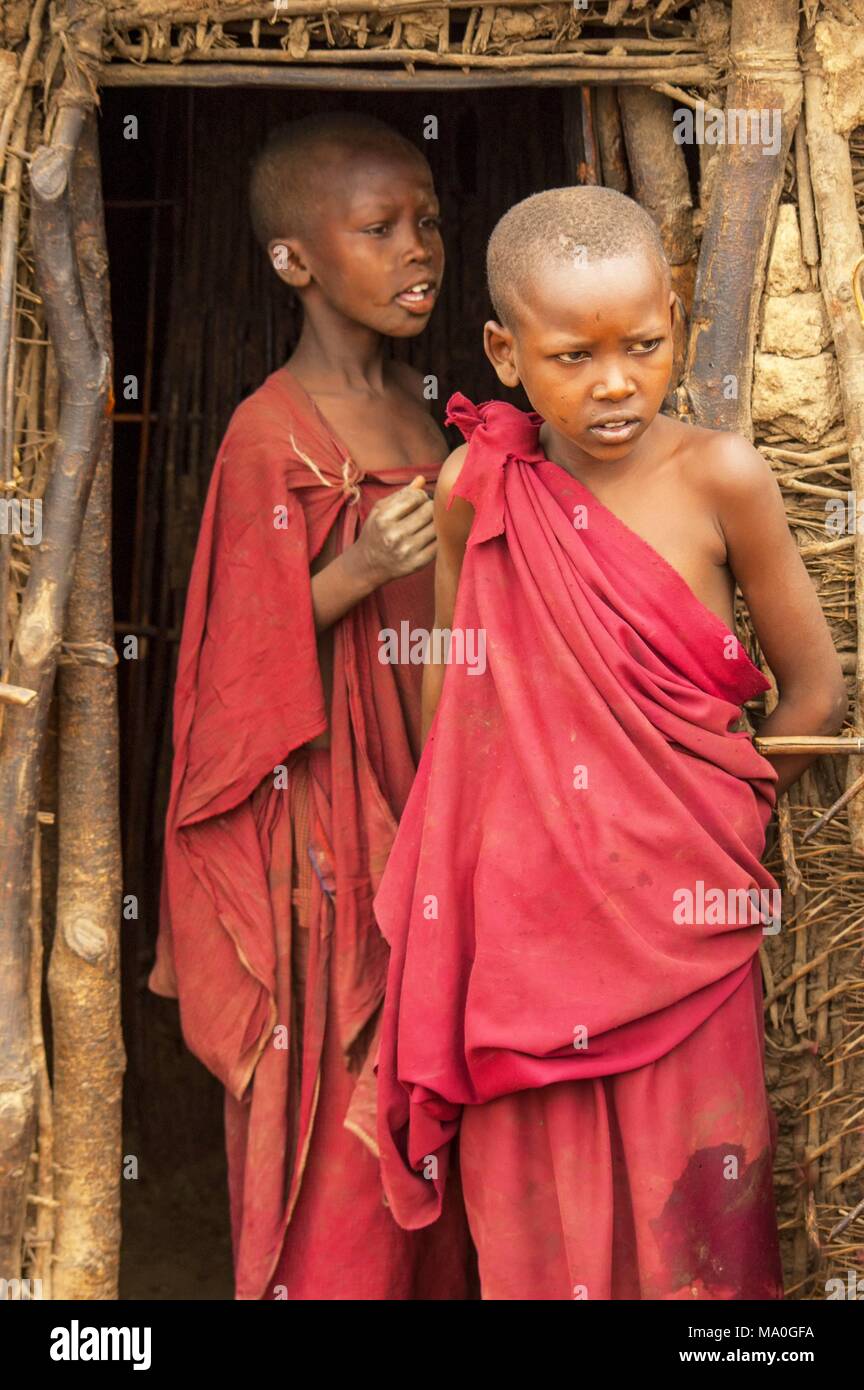 Masai giovani bambini presso l'entrata alle loro capanne in un tradizionale villaggio Massai, Kenya. Foto Stock