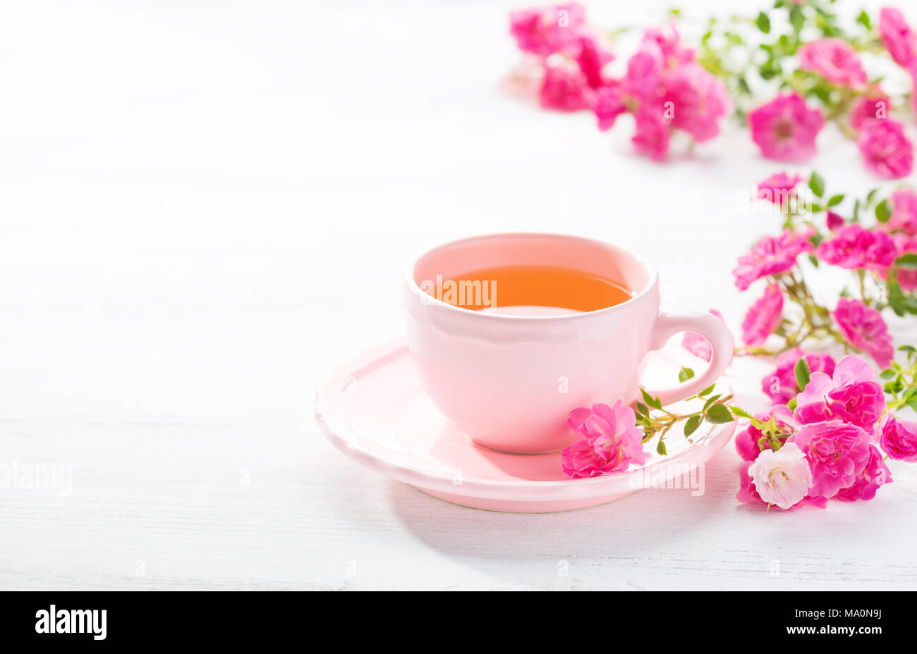 Tazza di tè e la filiale di piccole rose rosa su bianco tavolo rustico. Foto Stock