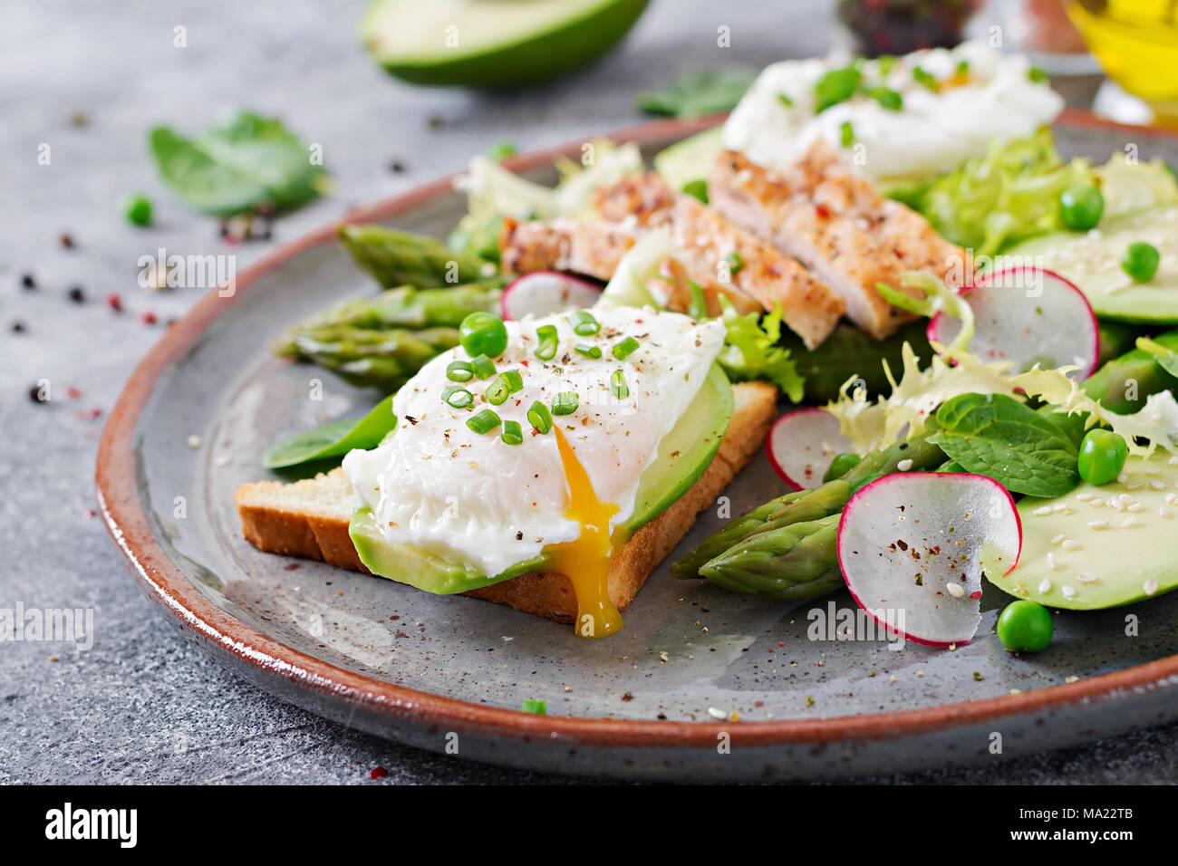 Una sana prima colazione. Uova in camicia su toast con avocado, asparagi e filetto di pollo alla griglia. Foto Stock