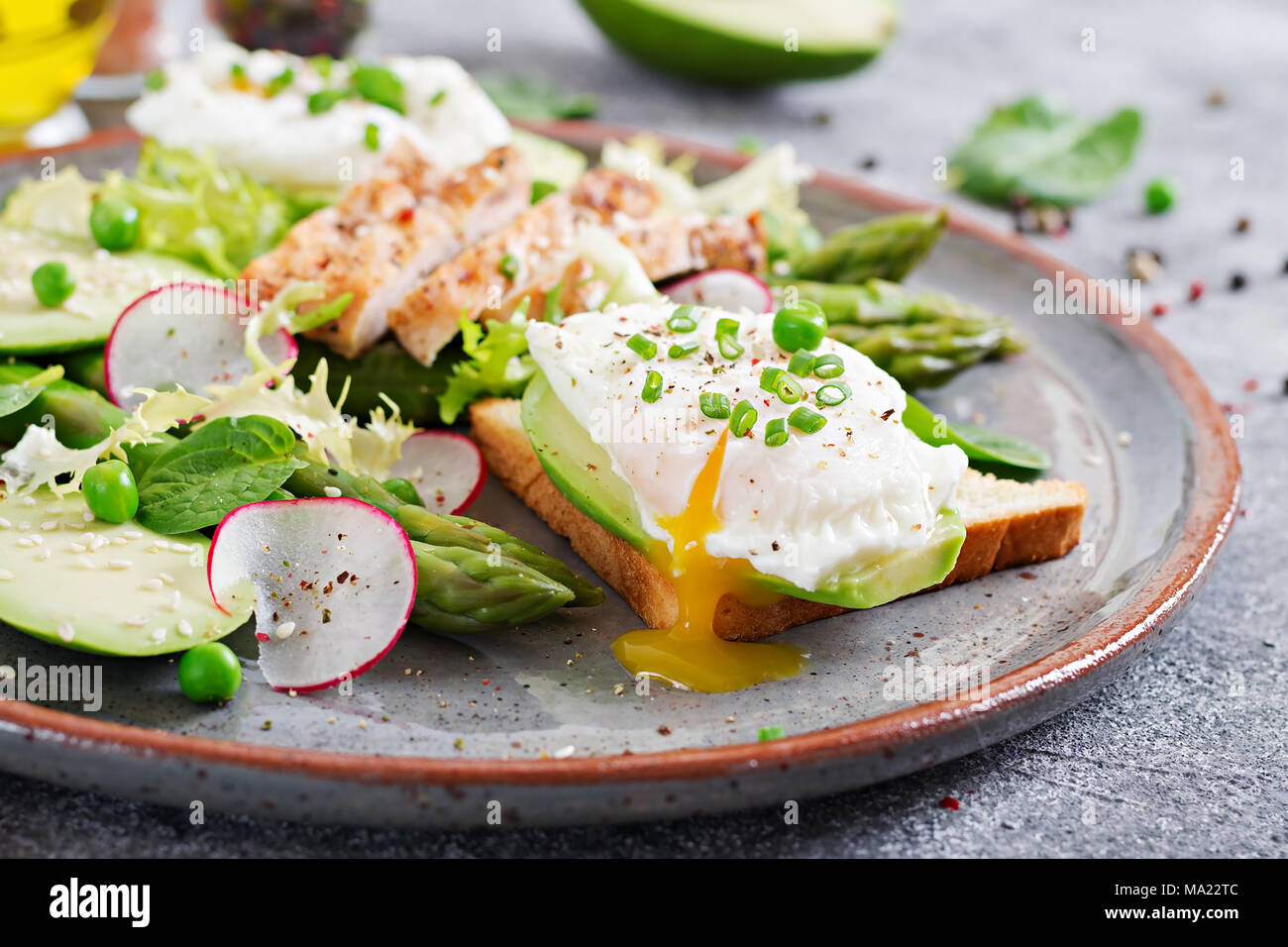 Una sana prima colazione. Uova in camicia su toast con avocado, asparagi e filetto di pollo alla griglia. Foto Stock