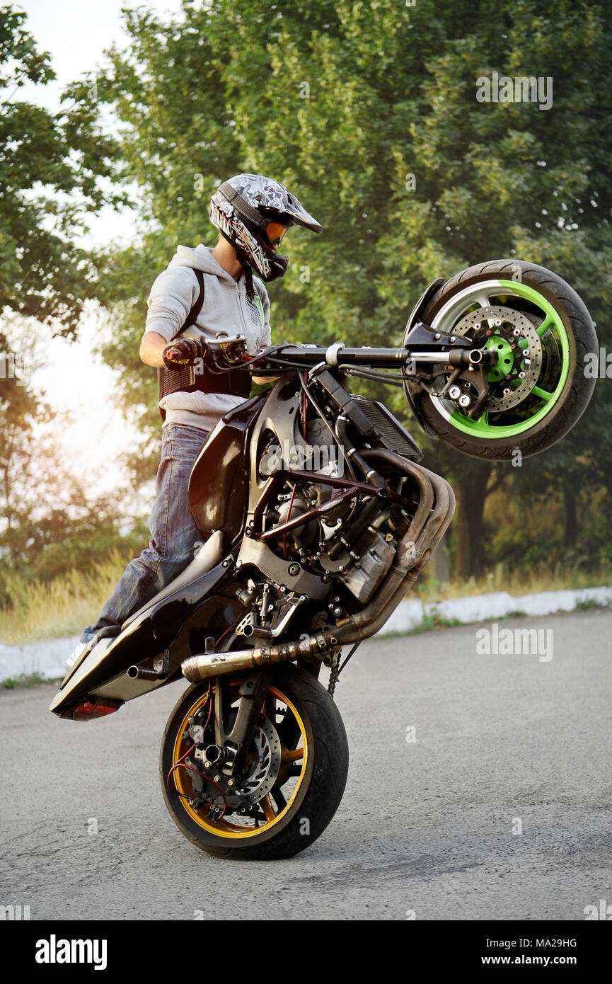 Ivano-Frankivsk, Ucraina - 28 Agosto 2015 : buona foto di uno stuntman facendo trick riding motociclo su un ciclo lungo la strada. Trucchi verde sullo sfondo. Tramonto d'estate. Foto Stock