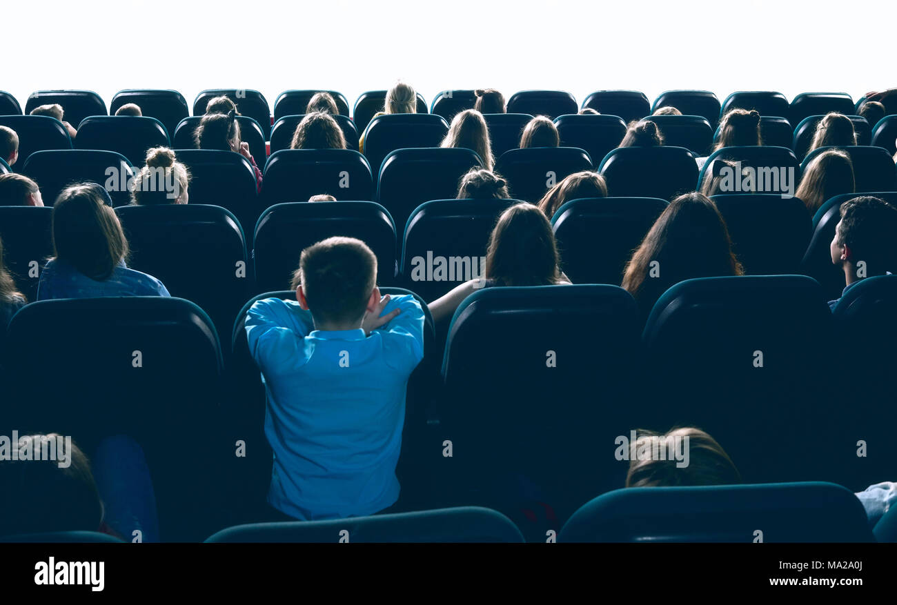 Un grande ammontare di gente a guardare il filmato nella grande sala cinema, seduti su confortevoli luoghi. Backview di donne, uomini e bambini intrattenimento cinema in casa. Foto Stock