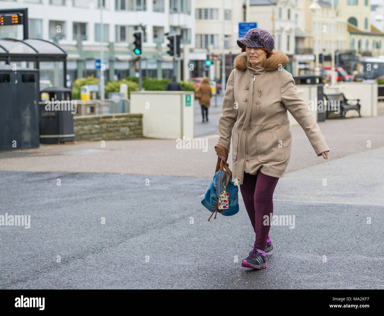 Active anziana signora vestita in una folta pelliccia e hat portando un sacco camminare veloce in tempo freddo. Foto Stock
